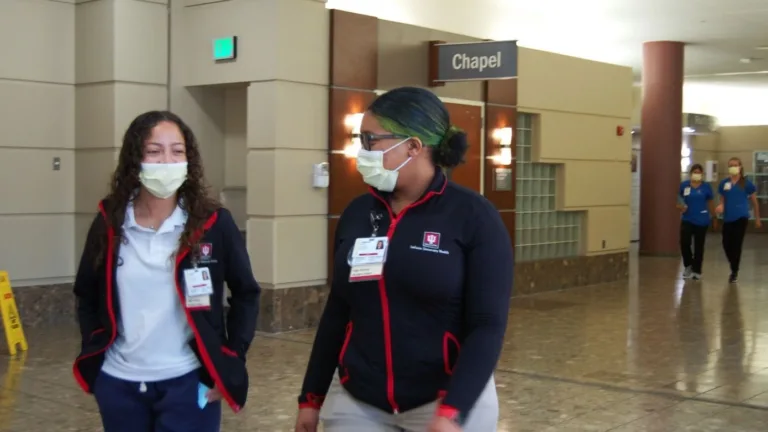 Two girls wearing masks and matching jackets walk down a hospital hall